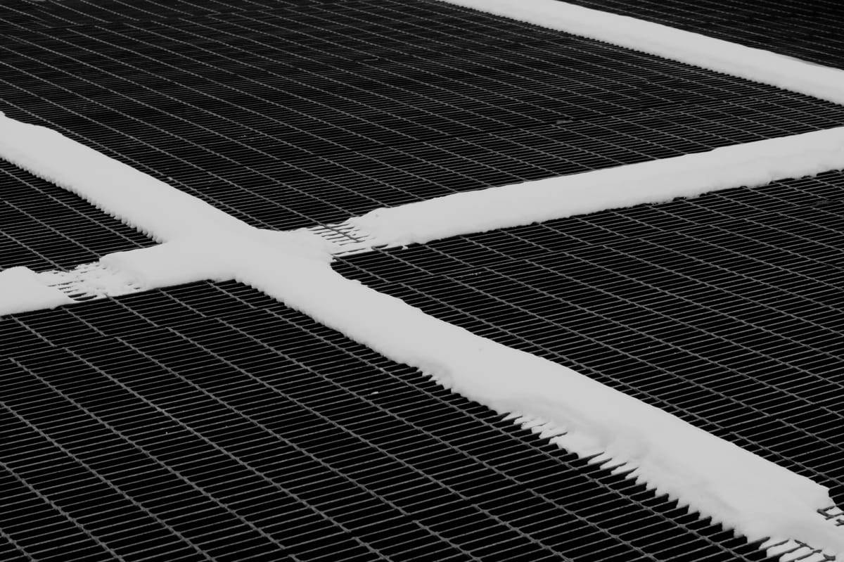 Black and white image of a grate with snow lining the connecting portions