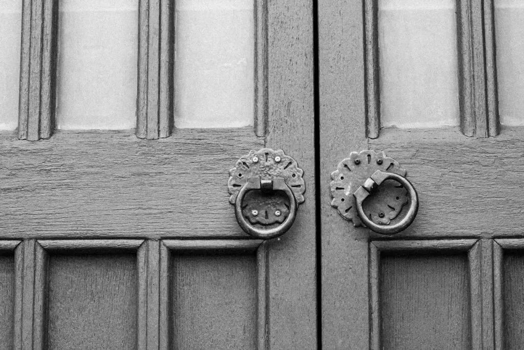 Black and white photo of a wooden door with metal hand grips instead of a handle.